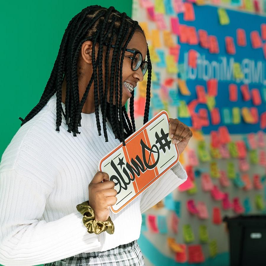 Student holds sign that says hashtag smile.